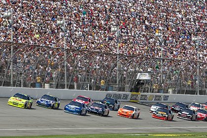 NASCAR race at Michigan International Speedway with cars racing in front of a packed grandstand